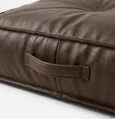Close-up of a dark brown -leather cushion with a built-in handle, showing the textured leather grain and stitching details.