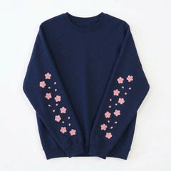 A navy blue crewneck sweatshirt with pink cherry blossom flower prints down both sleeves, laid flat against a white background.