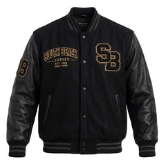 A black varsity-style jacket with black leather sleeves and black ribbed trim, featuring gold embroidered 'South Beach Leather' text and 'SB' lettering on the chest, and a gold number 9 on the sleeve.