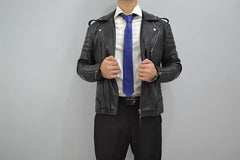 Person wearing a black leather jacket over a white shirt and blue tie on a gray background