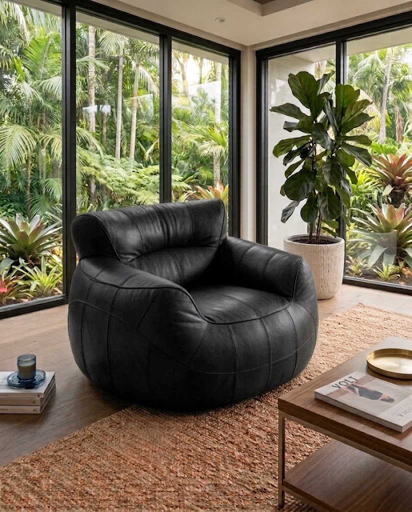 A modern black leather club chair with a tufted quilted design, placed in a stylish living room setting with large windows overlooking a lush tropical garden.