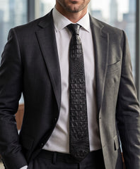 A man wearing a dark gray suit jacket, white dress shirt, and a black crocodile-embossed necktie, shown from the chest down in a professional office setting.