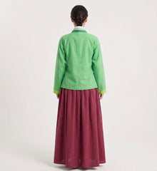 A woman shown from the back wearing a light green long-sleeve jacket with lime green cuffs and a long pleated burgundy skirt, set against a plain light gray studio background.