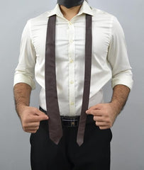 A man wearing a white long-sleeve button-up shirt, black trousers, and a dark brown wide tie, shown from the neck down against a plain gray background.