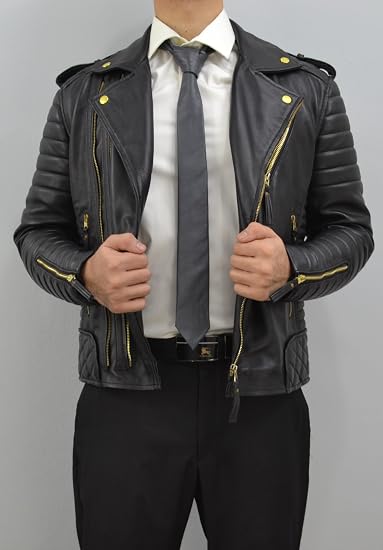 A man wearing a black leather motorcycle jacket with gold-tone zippers and snaps, styled with a white dress shirt, gray tie, and black trousers against a plain gray background.