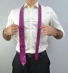 A man wearing a white dress shirt and black trousers models a bright purple necktie with a satin-like sheen, holding the collar area to show how it hangs.