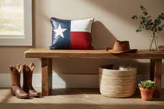 A rustic wooden bench in a styled room setting, featuring a Texas flag throw pillow, brown cowboy boots, a straw basket, and a small potted succulent.