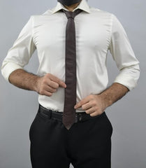 A man wearing a white long-sleeve dress shirt, a dark brown tie, and black trousers, shown from the neck down against a plain gray background.