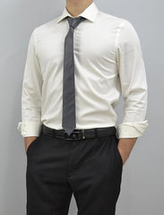 A man wearing a white long-sleeve dress shirt, a dark gray tie, a black belt, and black trousers, standing against a plain gray studio background.