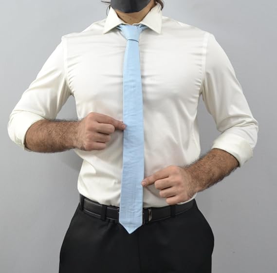 A man wearing a white long-sleeve dress shirt, a light blue necktie, and black trousers, adjusting the shirt collar and tie against a plain gray background.