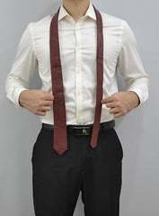 A man wearing a white long-sleeve dress shirt and black trousers, with a dark brown tie draped around his neck like a neck strap, against a plain gray background.
