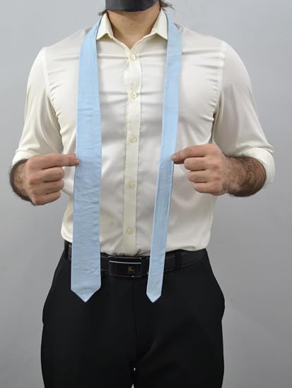 A man wearing a light blue necktie with a matching light blue neck scarf, styled with a cream dress shirt and black trousers against a plain gray background.