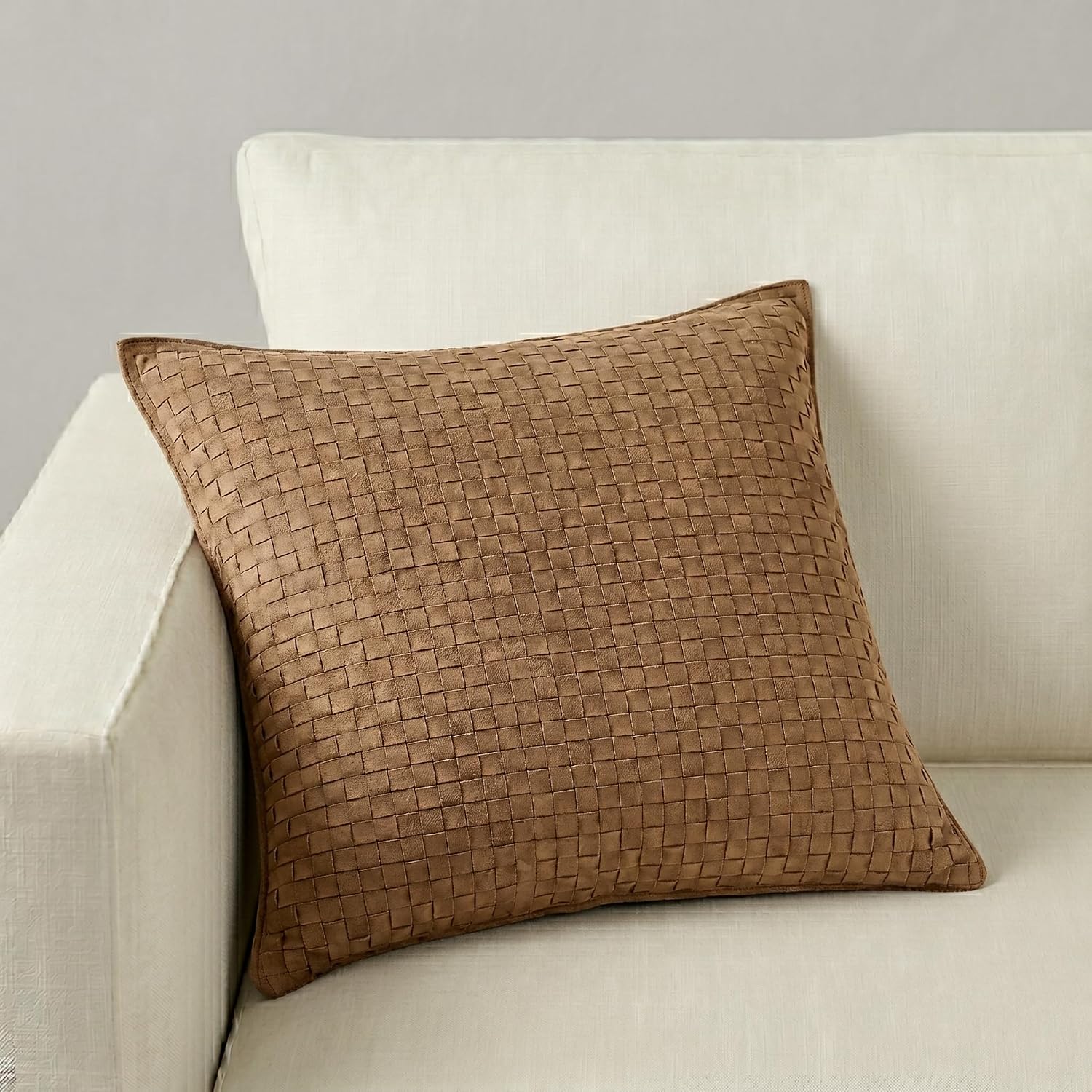 A square woven throw pillow in a warm brown tone, styled on a light beige fabric sofa against a neutral gray wall.