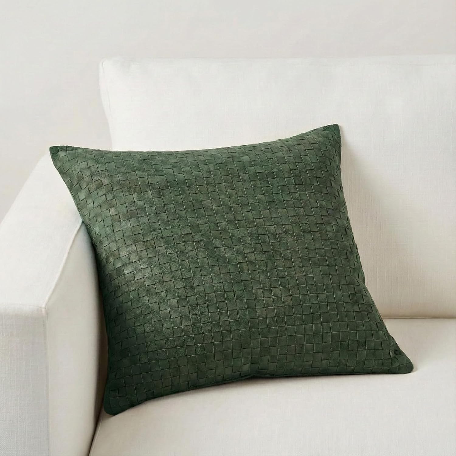 A square dark green woven throw pillow with a textured basketweave pattern, resting on a white fabric sofa.