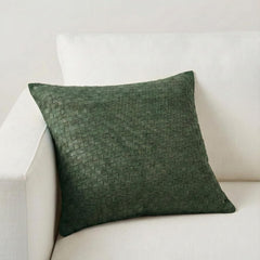 A square dark green woven throw pillow with a textured basketweave pattern, resting on a white fabric sofa.