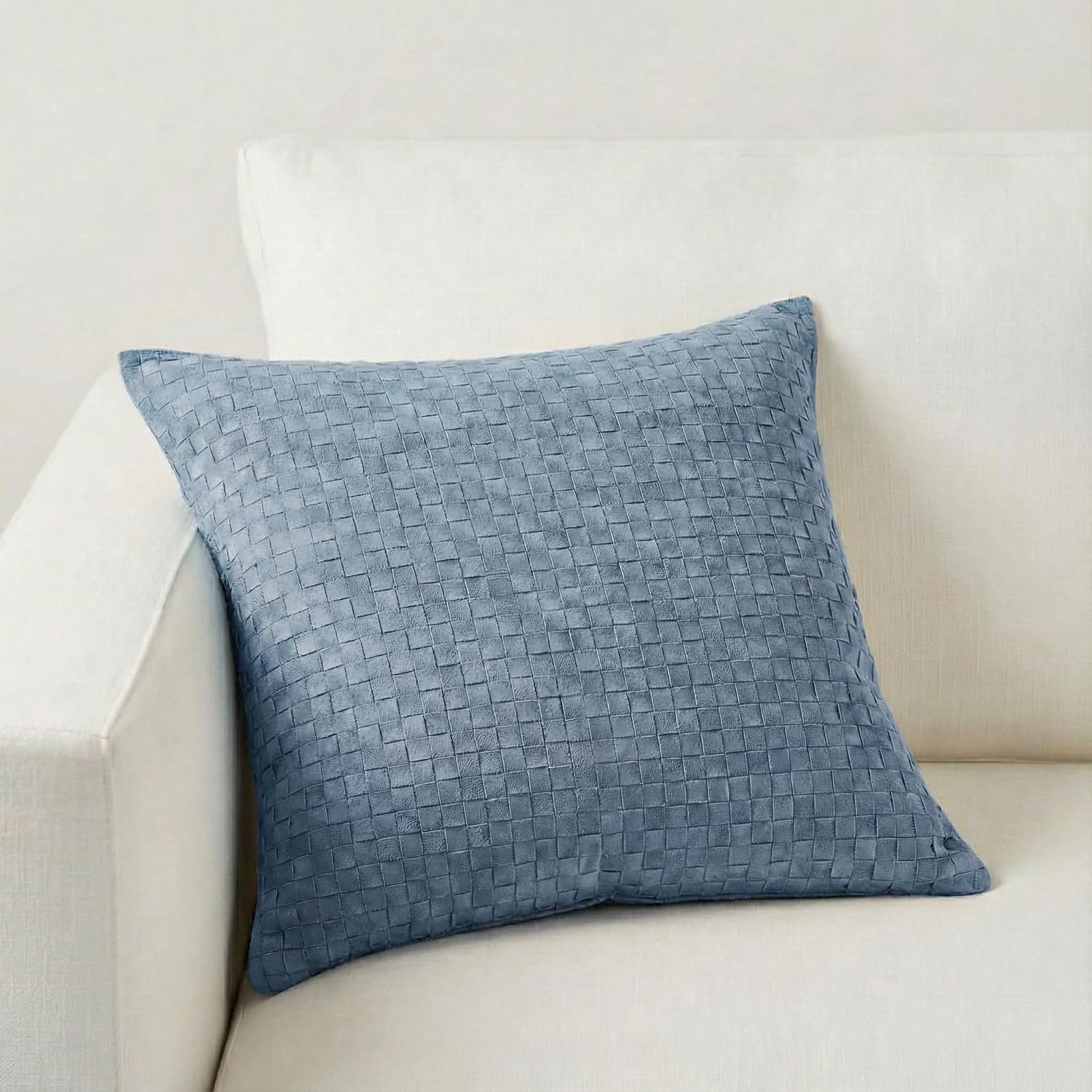 A square woven throw pillow in a dusty blue-gray color, styled on a light cream-colored sofa.