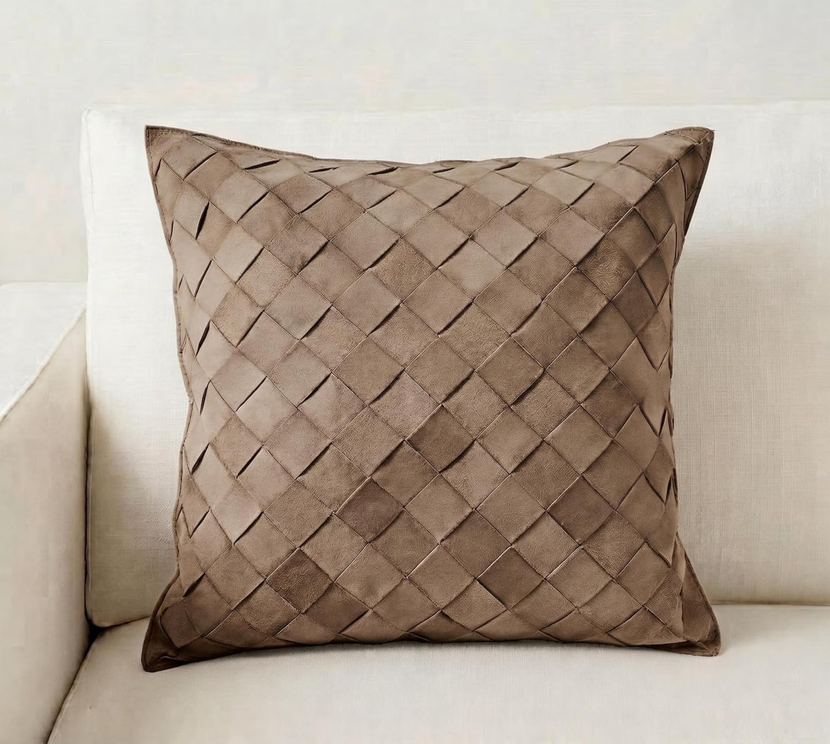 A square throw pillow in a taupe brown woven leather or faux-leather material, displayed on a light beige sofa.