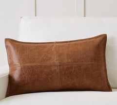 A rectangular brown leather lumbar pillow with a natural distressed texture, resting on a white upholstered sofa.