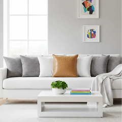A modern white sofa in a bright living room, styled with gray and tan accent pillows, a white throw blanket, a white coffee table with a small plant and colorful books, and framed abstract wall art.