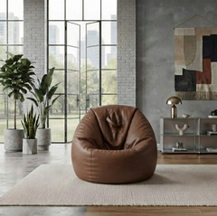 A brown leather bean bag chair placed on a light beige rug in a modern industrial-style room with large windows, plants, and a small shelving unit.