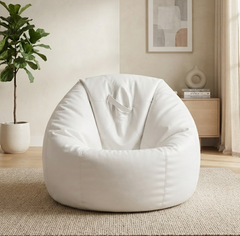 A large white bean bag chair with a fabric sling seat, placed on a woven rug in a bright, modern living room setting.