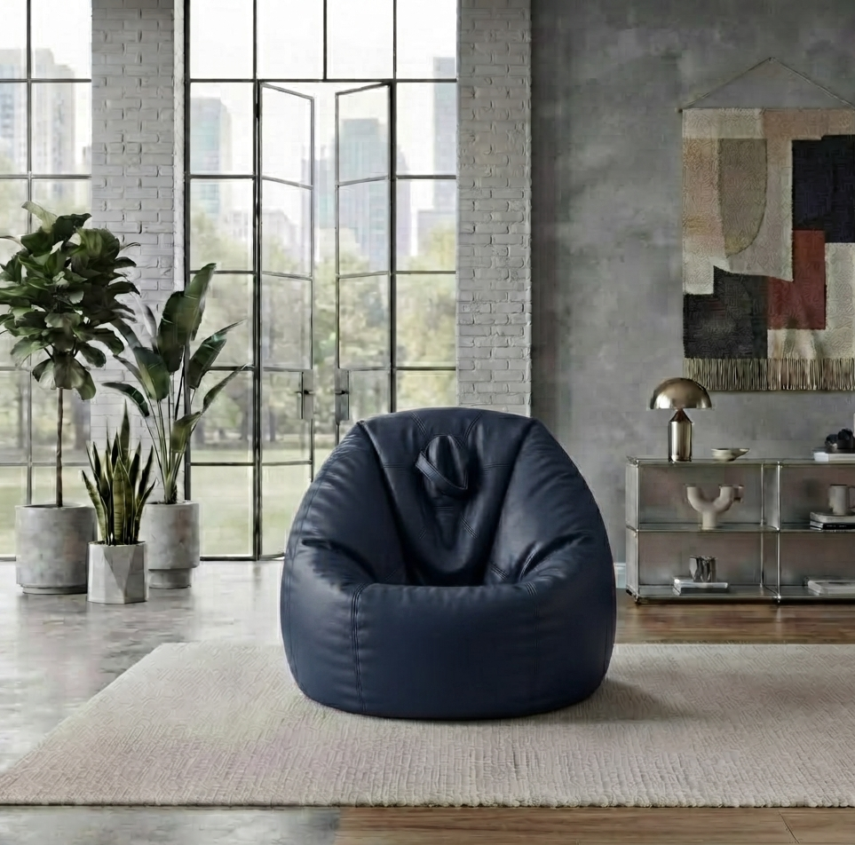 A dark navy blue bean bag chair placed on a light beige rug in a modern loft-style room with large industrial windows, brick walls, potted plants, and a side table.