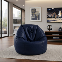 A large, plush navy blue bean bag chair made of faux leather, styled in a modern living room setting on a light beige rug.