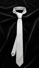 A light gray textured necktie with a wide collar and a loose knot, displayed on a draped black satin fabric background.