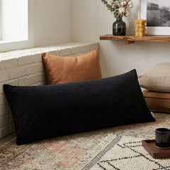 Black rectangular pillow on a textured rug with a cozy living room setting.
