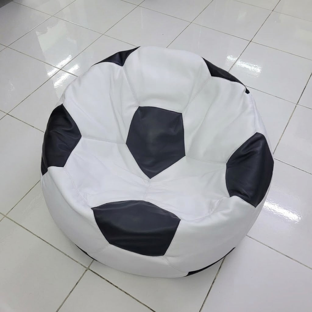 A round bean bag chair designed like a soccer ball, featuring a white body with black pentagonal panels, placed on a glossy white tiled floor.