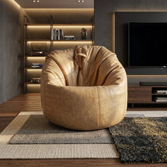 A round, low-profile tan leather armchair or beanbag-style chair placed in a modern living room with wood flooring, layered rugs, shelving, and a television in the background.