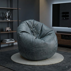 A large, rounded gray faux-leather bean bag chair with a distressed texture, styled in a modern living room setting on a round rug.