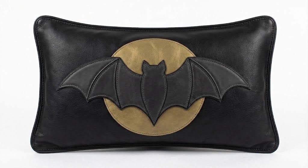 Matte black leather lumbar pillow cover featuring a dimensional bat silhouette layered over an antique gold-toned leather full moon, finished with charcoal edge stitching, shown against a white background.