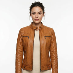 A woman modeling a tan leather motorcycle jacket with a stand collar, zippered chest pockets, and zippered side pockets, worn over a cream top against a plain white background.