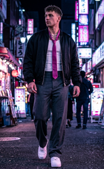 A man walking down a neon-lit city street at night, wearing a black bomber jacket, white shirt, bright pink tie, dark gray trousers, and white sneakers.